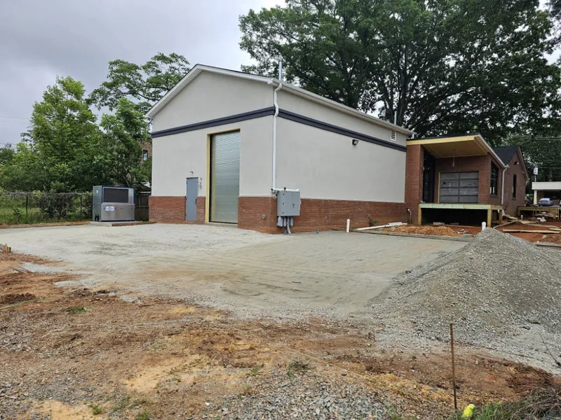 Single-story commercial building with stucco walls and a roll-up door beside a freshly graded gravel lot