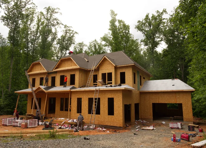 Crew working on the sheathed roof deck of a framed two-story house under construction