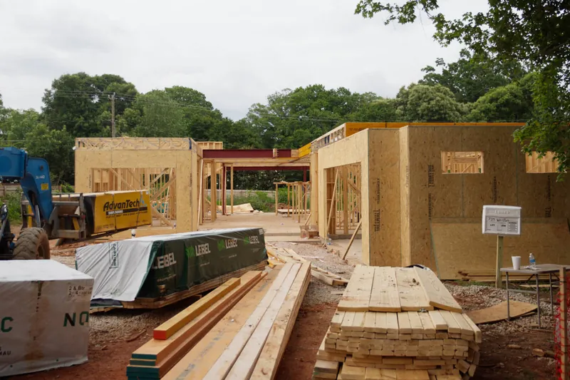 Bundles of framing lumber staged in front of framed walls on a job site