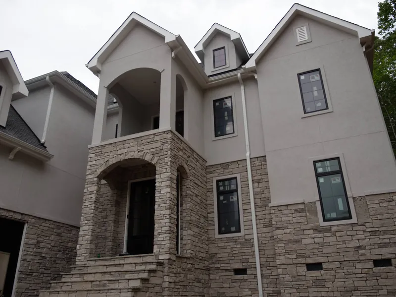 Side elevation of a stucco and stone custom home showing the arched balcony and dormers