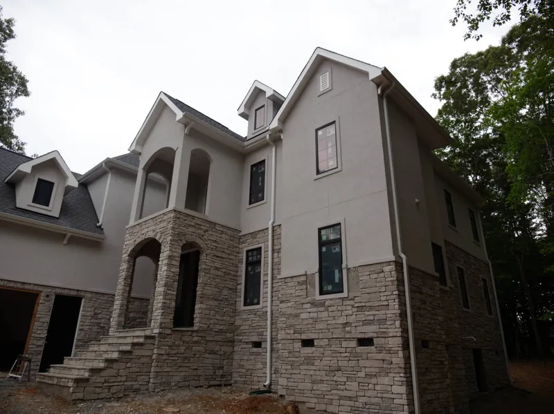 Rear corner of a stucco and stone custom home under construction with new gutters and downspouts