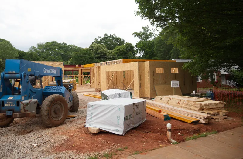 Telehandler unloading sheathing beside a framed building on a construction site